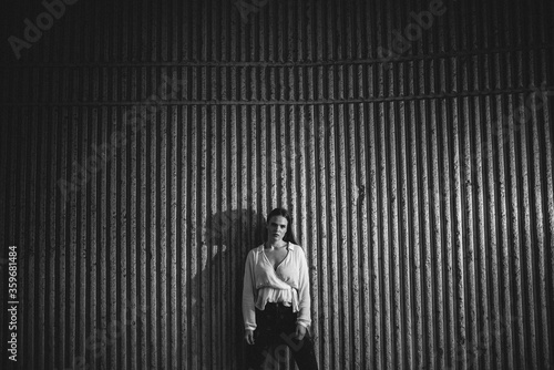 A black and white picture of a beautiful young caucasian girl in a white shirt in front of a ribbed wall