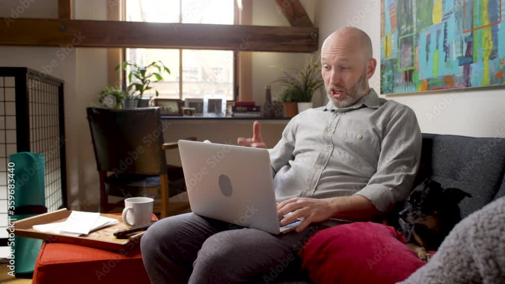 A man working from home video chats with his laptop while sitting on the couch with his cute chihuahua A man working from home video chats with his laptop while sitting on the couch with his cute chihuahua