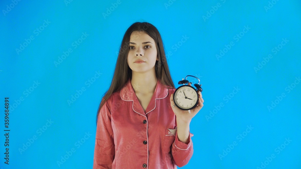 Sleepless woman in pajamas pointing at alarm clock