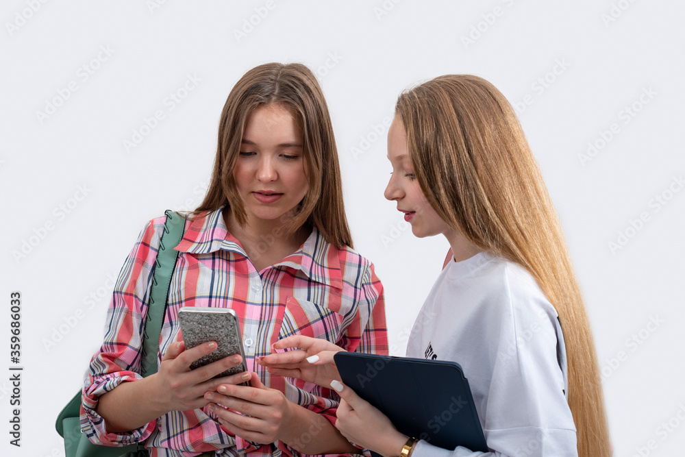 Teenage schoolgirls with backpacks and a tablet are walking together, isolated Teenage schoolgirls with backpacks and a tablet are walking together, isolated
