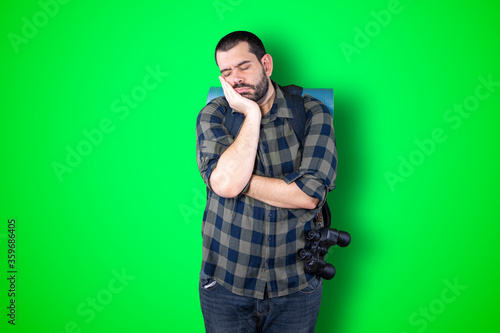 Bored young bearded traveler guy over green studio background