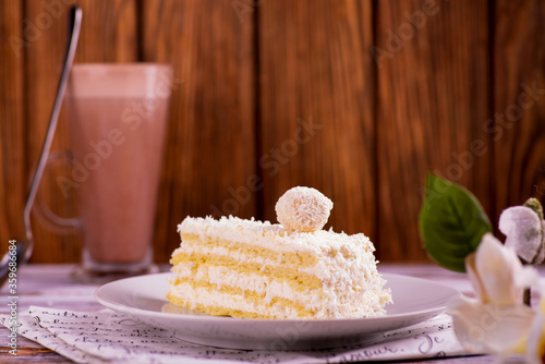 cake with coconut and raffael ball on a white plate on a background of chocolate milk on a wooden background photo