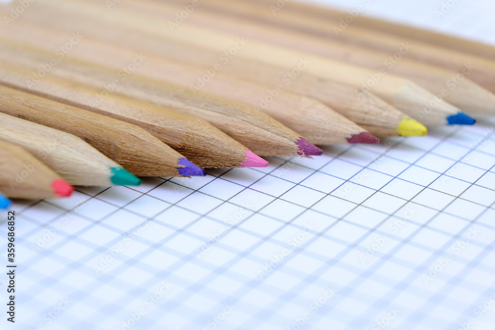 Closeup set of multicolored pencils on the checkered paper sheet of notebook for the drawing. Back to school concept. Closeup set of multicolored pencils on the checkered paper sheet of notebook for the drawing. Back to school concept.