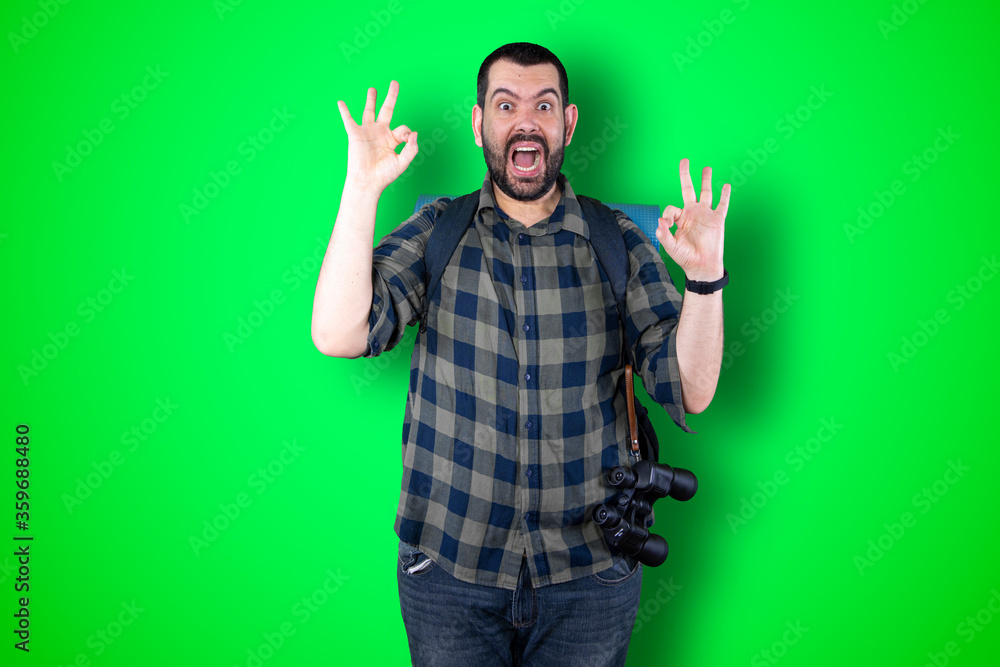Fototapeta premium Portrait of a cheerful young traveler man showing okay and victory gesture isolated on the chroma background