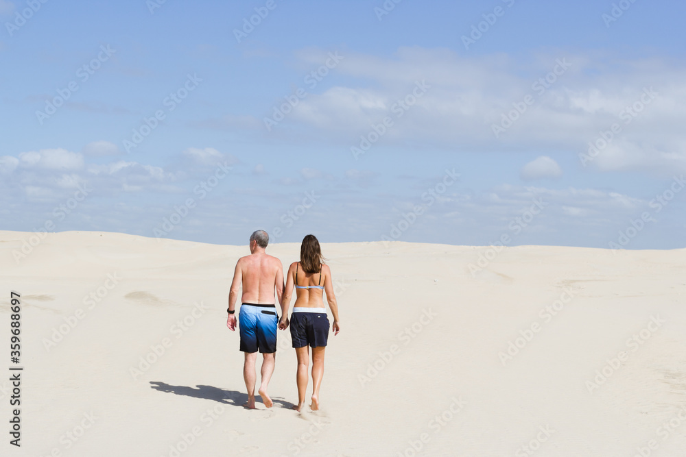 Rear view of caucasian  couple walking hand in hand up sand dune.