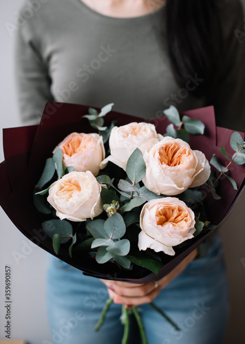 Very nice young woman holding huge beautiful blossoming mono bouquet of fresh David Austin roses in tender pink colors and eucalyptus on the grey background