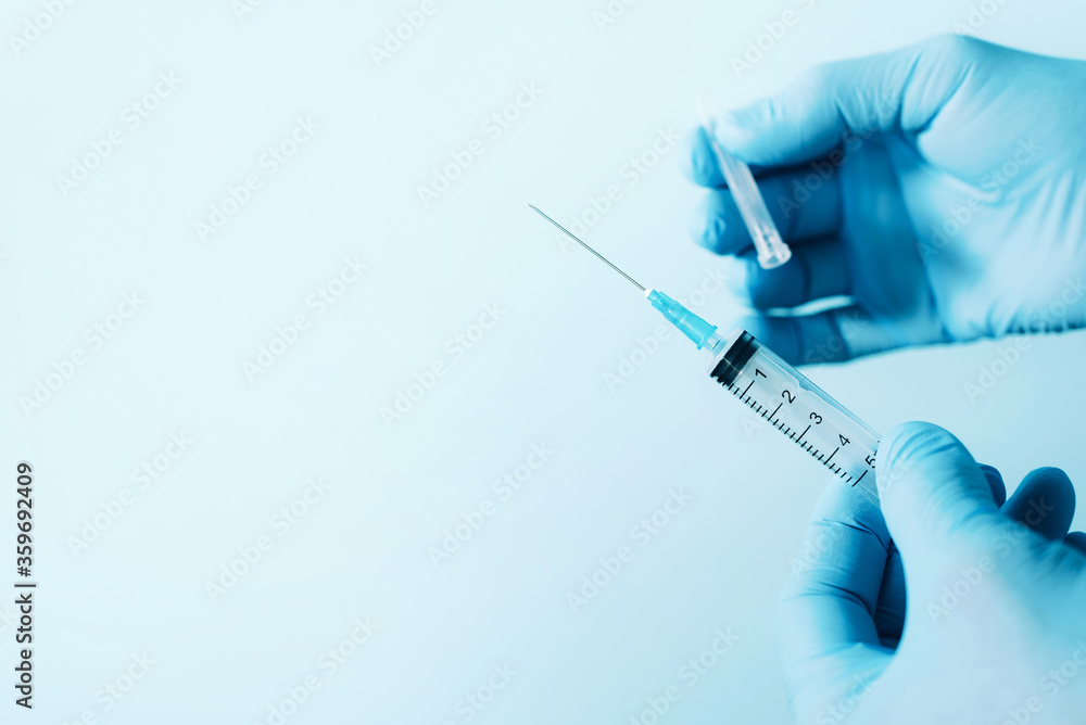 Hand in medical gloves holding syringe on blue background. Copy space. Injections and vaccination concept. Health protection equipment during quarantine Coronavirus pandemic Hand in medical gloves holding syringe on blue background. Copy space. Injections and vaccination concept. Health protection equipment during quarantine Coronavirus pandemic