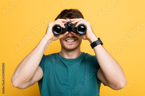 cheerful man looking through binoculars on yellow photo
