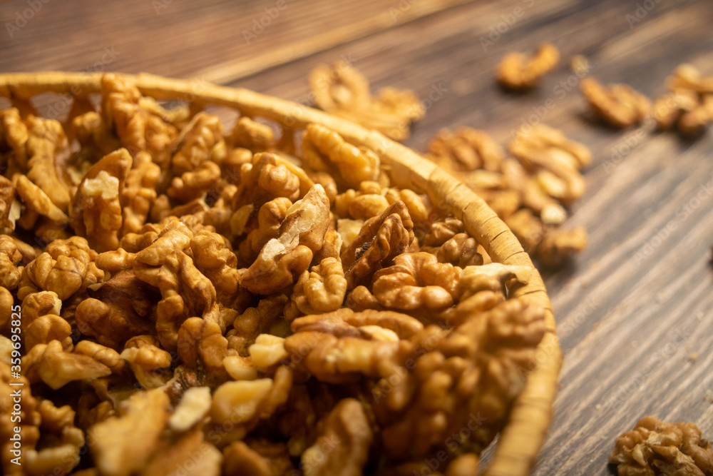 Obraz premium Peeled walnuts in a wicker basket and peeled walnuts scattered on a wooden table. Healthy diet. Fitness diet. Close up.