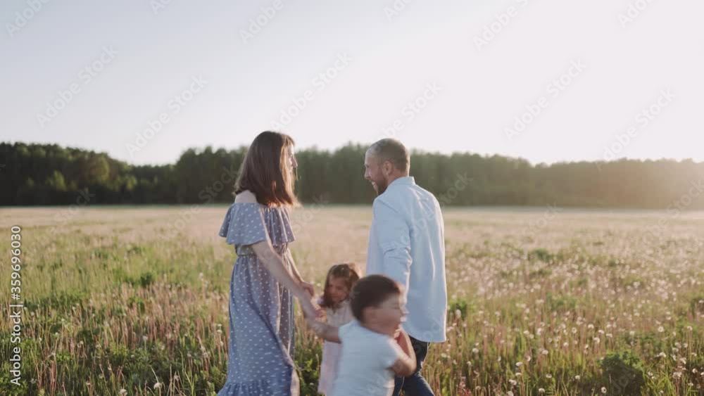 Man and woman and two kids are dancing on the field during sunset. Husband and wife love each other. Happy family spend time together. Relaxing outside. Family value. Man and woman and two kids are dancing on the field during sunset. Husband and wife love each other. Happy family spend time together. Relaxing outside. Family value.