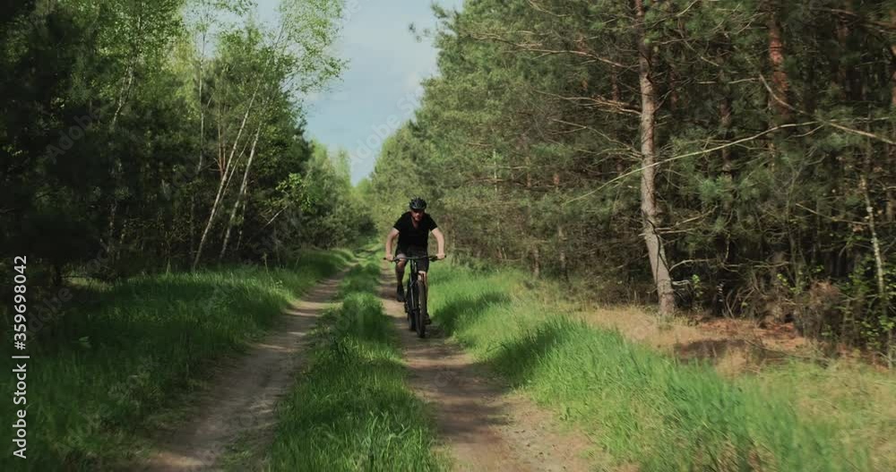 Cyclist rides on a forest road. Man on a mountain bike rides in the forest. Adult man in a bicycle helmet rides on a mtb bicycle in the summer. Cyclist rides on a forest road. Man on a mountain bike rides in the forest. Adult man in a bicycle helmet rides on a mtb bicycle in the summer.
