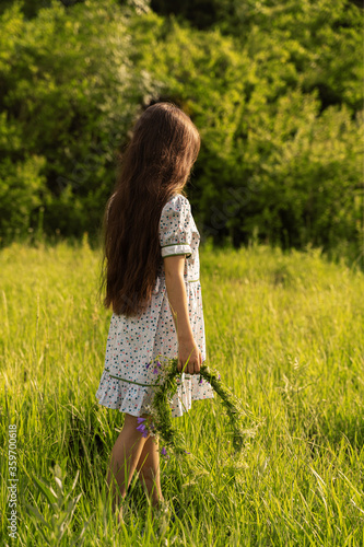 a girl holds a wreath of flowers. rear view. sunset