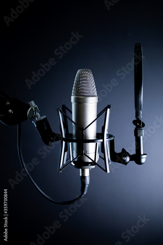 Condenser podcasting microphone in dramatic light with pop filter on black background