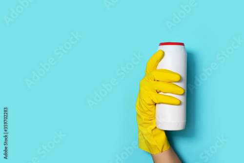 Hand in glove holding white plastic bottle of cleaning product, household chemicals. Copy space. Cleaning service concept. Household chemical cleaning products, brushes and supplies. Detergent bottle