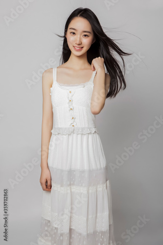 Asian girl with long fluttering hair wearing white skirt in gray background