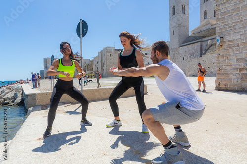 Due amiche fanno sport sulla spiaggia di una città di mare mentre il ragazzo giovane muscoloso da lezioni di plank mostrando loro l'esercizio di atletica libera
