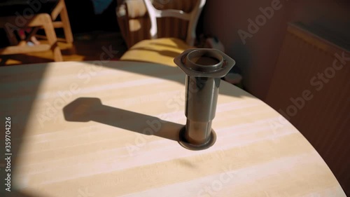 An aeropress brewing fresh coffee on a wooden table in the sunlight with its shadow next to it. photo