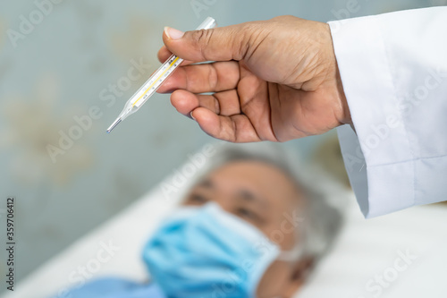 Doctor holding thermometer to measures asian senior or elderly old lady woman patient wearing a face mask have a fever in hospital   healthy strong medical concept.