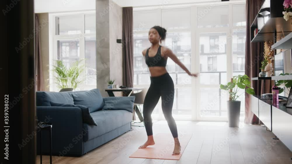 Fit african american sportswoman performing swuats and jumps exercising warming-up cardio training sports routine in the living room. Home isolatio. Fitness. Workout. Fit african american sportswoman performing swuats and jumps exercising warming-up cardio training sports routine in the living room. Home isolatio. Fitness. Workout.