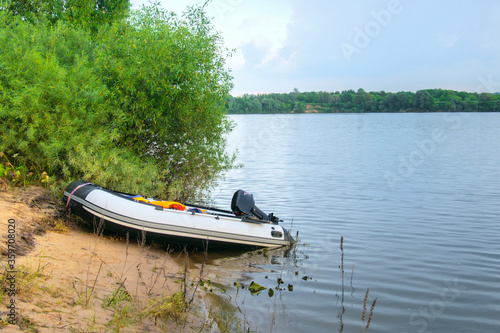 white motorized PVC inflatable boat moored on the sandy shore of the lake against a cloudy sky