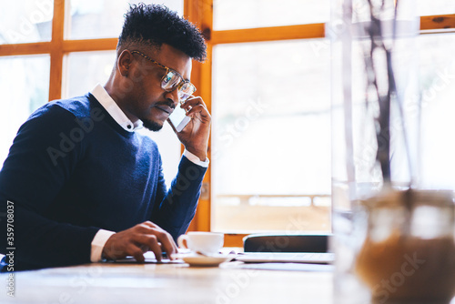 Confident well-dressed afro american entrepreneur having phone conversation with managers controlling work on new startup while waiting for meeting with journalists to give interview about career
