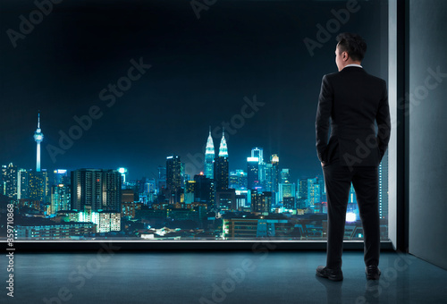Young businessman standing in front full-length window looking at cityscape with skyscrapers. Business concept considering and inspiration moment.