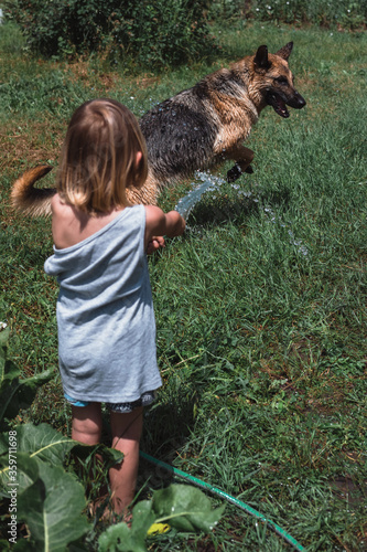 A small boy plays with a dog, watering it with a hose