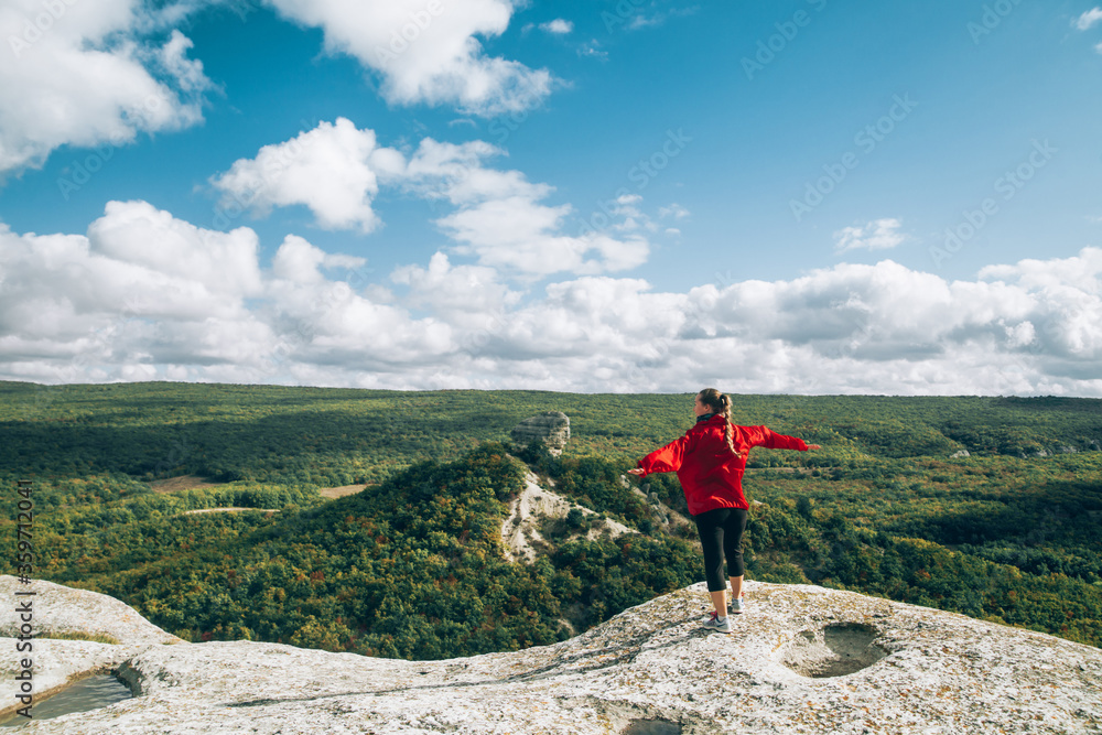 A young girl stands on top of a mountain and raises her hands.