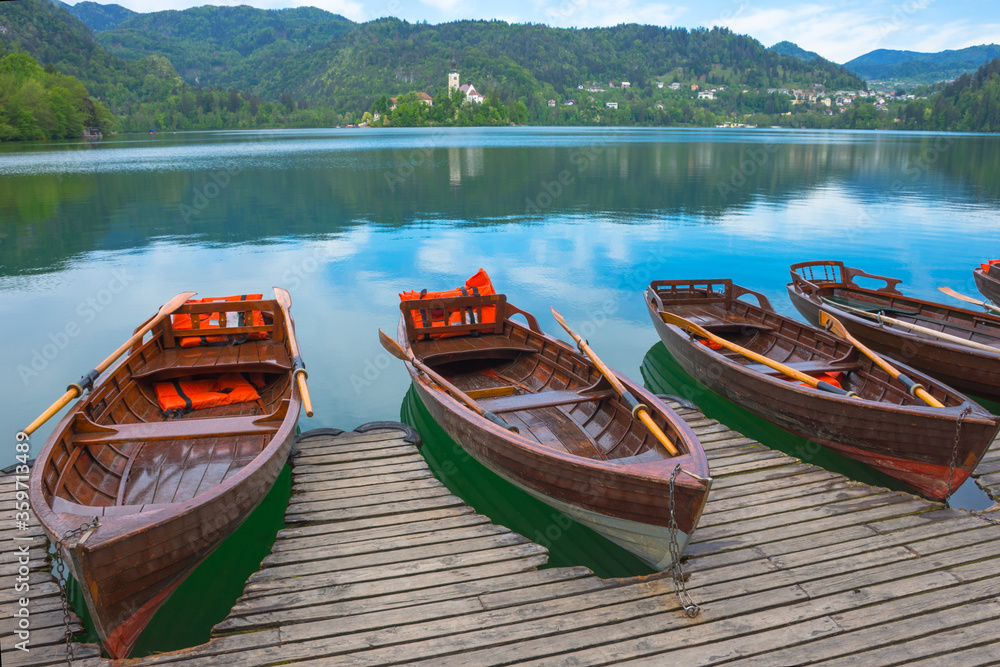 Traditional boats waiting for tourists on Lake Bled, with the lake island and charming little church in the background, famous tourists attraction in Slovenia