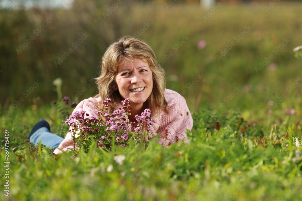 Senior woman lying in the grass with flowers around her Senior woman lying in the grass with flowers around her