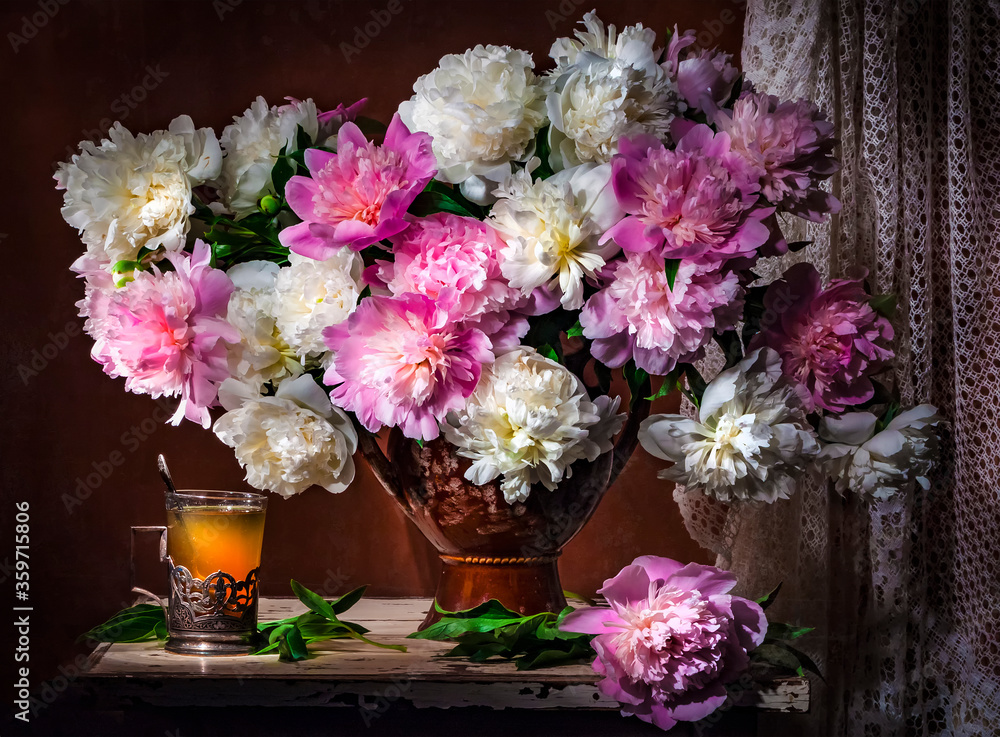 Classic still life with bouquet of beautiful white and pink peonies and a glass of tea in a Russian glass holder a ray of light on brown background . Art photography. Classic still life with bouquet of beautiful white and pink peonies and a glass of tea in a Russian glass holder a ray of light on brown background . Art photography.