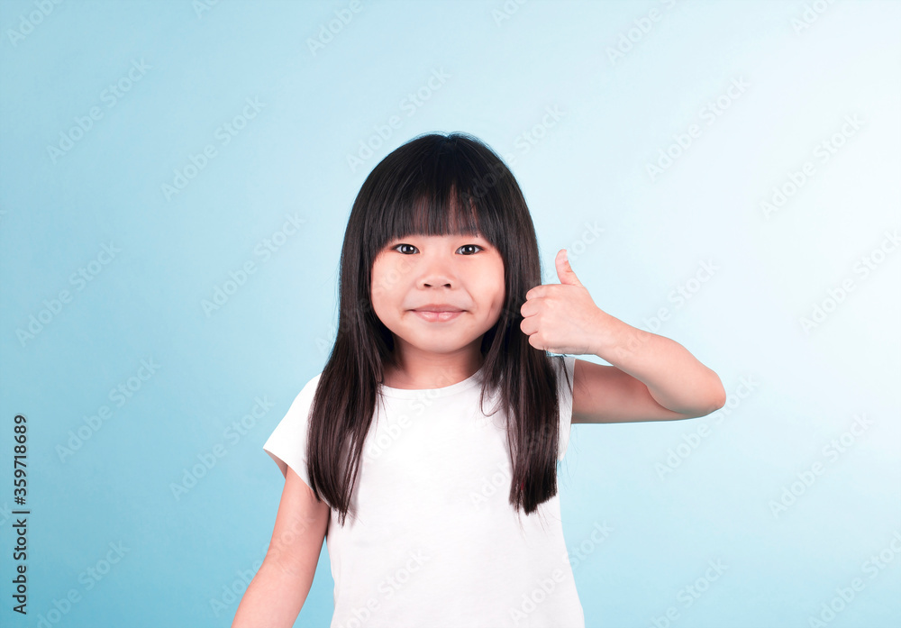 Studio portrait of a cute asian little girl with posing. happy with big smile doing ok sign, thumb up with fingers, excellent sign. isolated in blue background. Studio portrait of a cute asian little girl with posing. happy with big smile doing ok sign, thumb up with fingers, excellent sign. isolated in blue background.