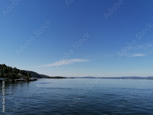 Beautiful calm day on the sea with clear blue sky and island with pine trees