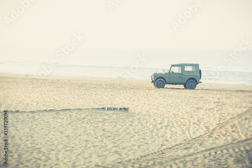 Vintage jeep parked on a deserted beach at sunrise in summer time , clear sky with no clouds , holiday scene photo