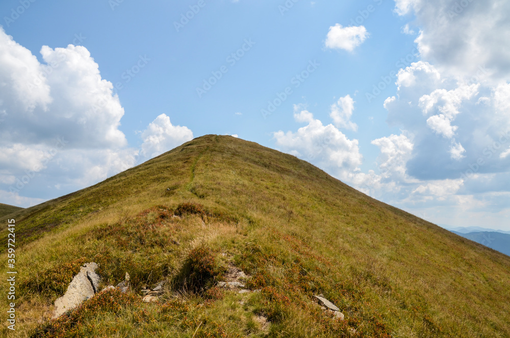 Grassy peak with hillside under clouds in summer warm day. Tyapesh mountain top in Carpathian, Ukraine.
