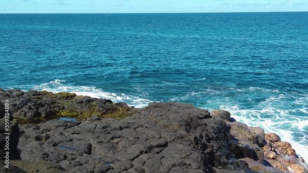 HD Hawaii Kauai slow motion slight pan right to left wide shot of ocean waves swirling and crashing on lava rock in lower half splashing up in center frame with blue sky on ocean horizon HD Hawaii Kauai slow motion slight pan right to left wide shot of ocean waves swirling and crashing on lava rock in lower half splashing up in center frame with blue sky on ocean horizon