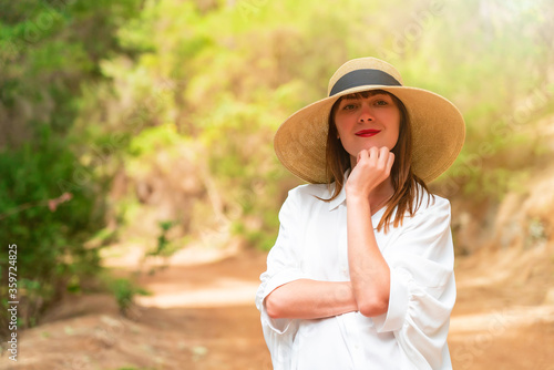 Portrait of a redhead woman in white dress and hat in the forest on a sunny day.