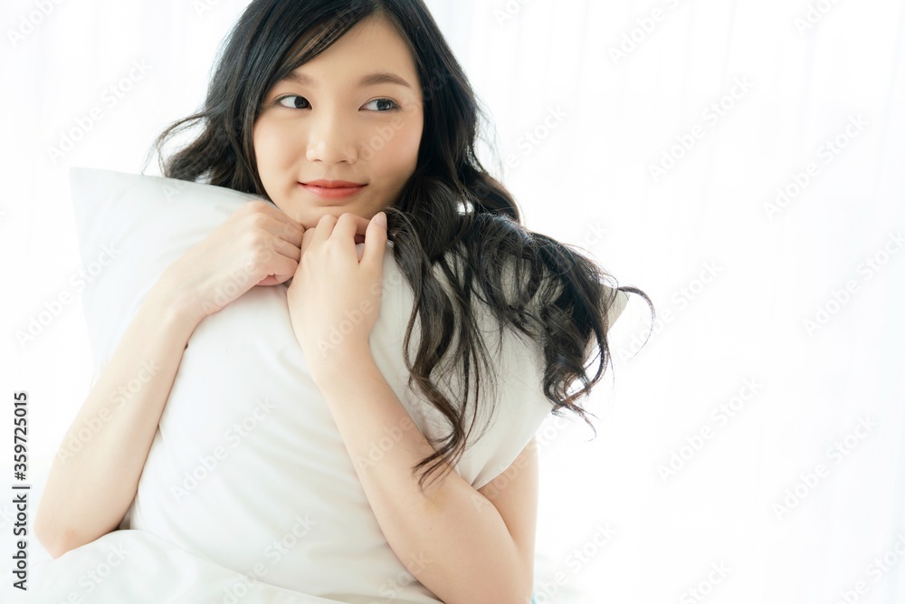 Young and beautiful Asian woman hugging a pillow with smile on her bed in front of curtain. Young and beautiful Asian woman hugging a pillow with smile on her bed in front of curtain.