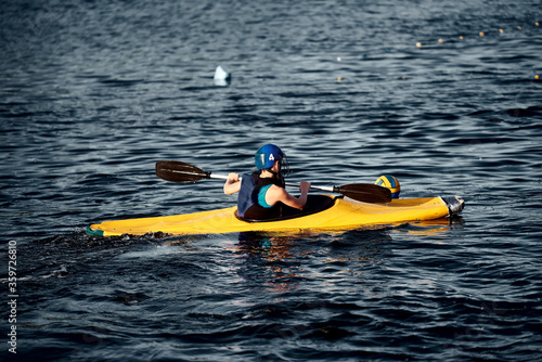 A guy wearing a helmet on a canoe polo rowing a paddle and sailing on water. canupolo. puts on a rescue yellow. rear view. water splashes