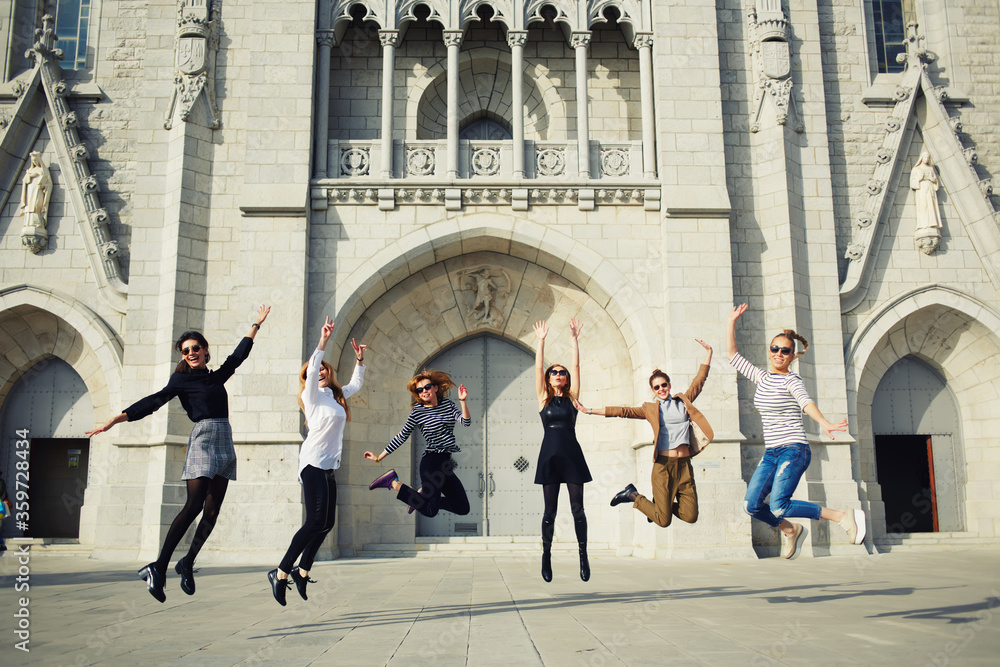 Portrait of a lively excited women jumping in air against building, enjoying holidays, group of girlfriends outdoors having lots of fun jumping around