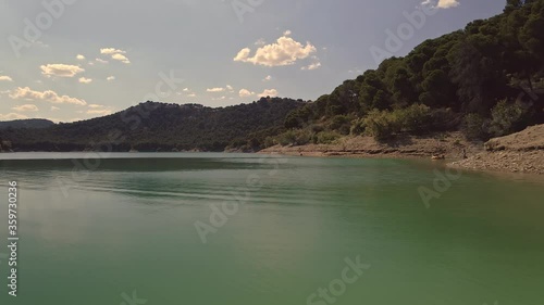 Calming tranquil aerial scene from shoreline across peaceful shimmering mountain valley lake water surface
