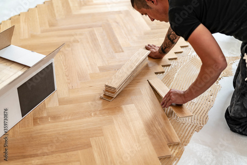 Handwerker verlegt einen atemberaubenden Parkettboden im Fischgräten Muster und setzt gerade ein frisches Brett an