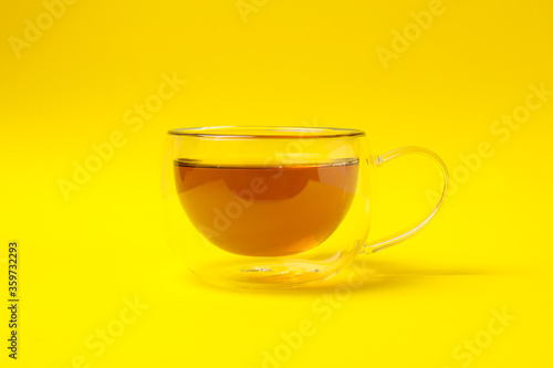 Glass cup of chamomile tea on yellow background