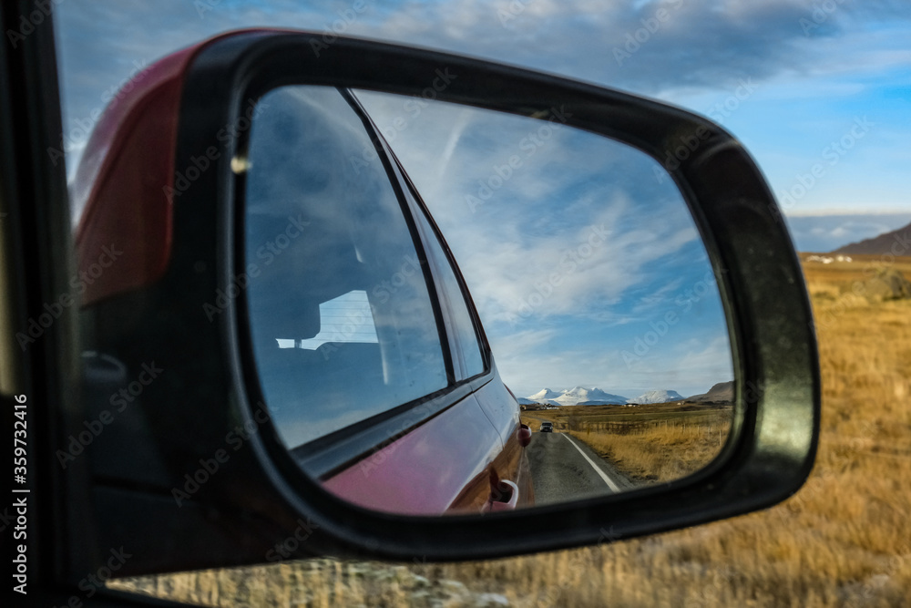 reflection in the rearview mirror. landscape with a road, mountains, field and car. Iceland. road trip individual travel