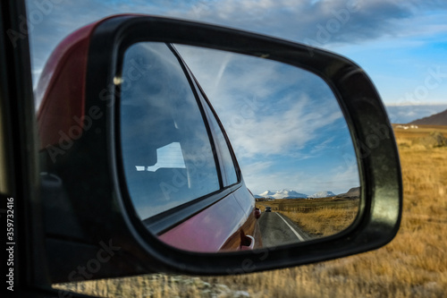 reflection in the rearview mirror. landscape with a road, mountains, field and car. Iceland. road trip individual travel