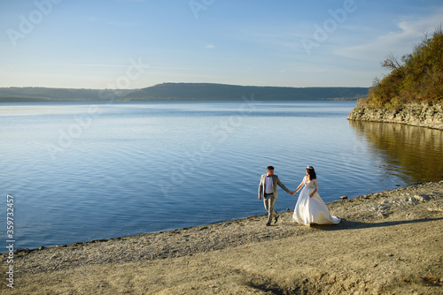 The bride and groom are walking near the lake on the shore. © wolfhound911