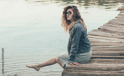  The girl is sitting on a post near the river, the girl is wetting her feet in the river and smiling © Катя Данилюк