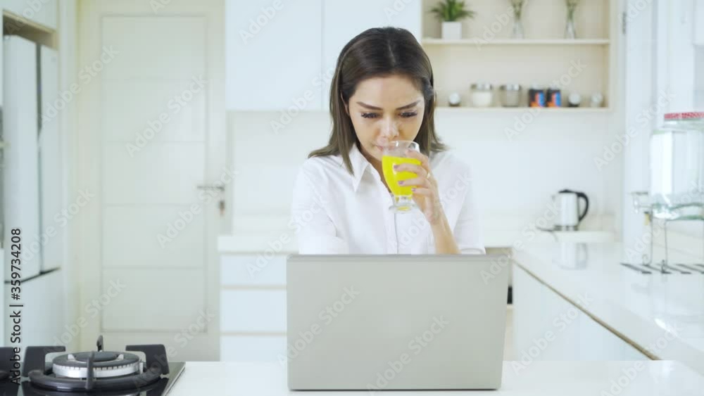 Woman works with laptop while drinks orange juice Woman works with laptop while drinks orange juice