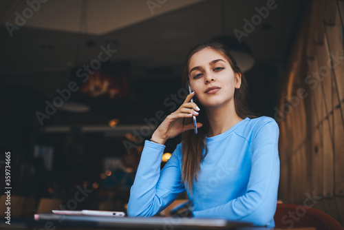 Portrait of charming confident female in cool spectacles for good vision looking at camera while chatting with followers and sharing news in social networks on cellular connected to 4G