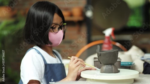 Selective focus on clay work with defocused young girl painting on the pot
